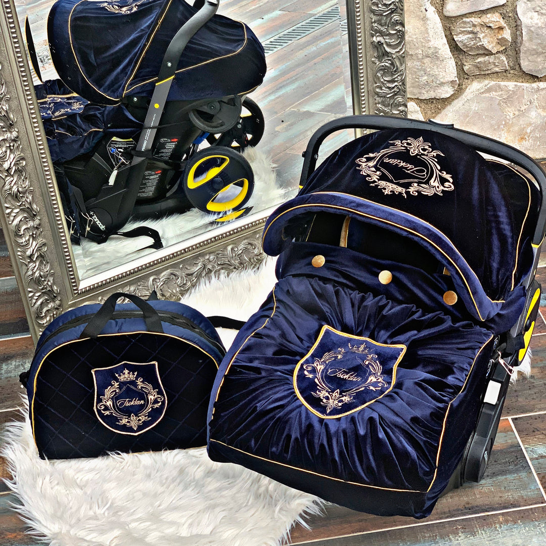 Image of royal blue velvet baby car seat cover set for Graco, adorned with gold personalized embroidery on the hood, footmuff, and diaper bag. Matching accessories feature luxurious gold elements.