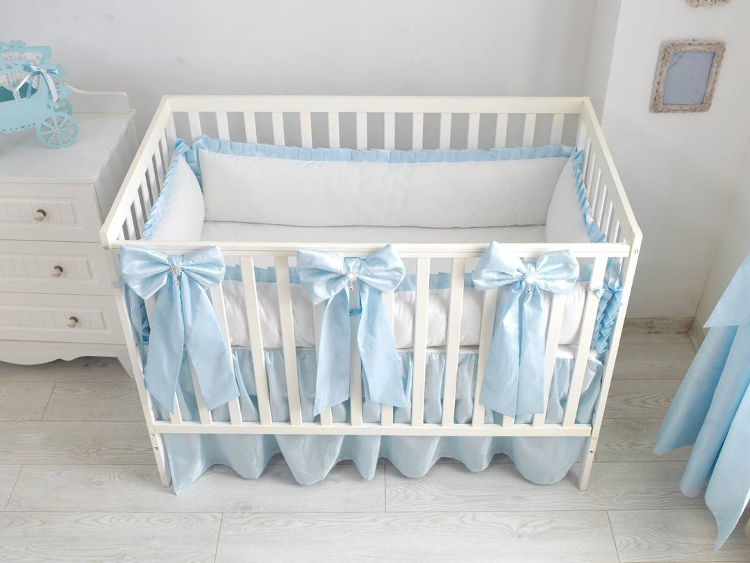 An elegant white crib bedding set featuring a large, perfectly tied bow on the crib skirt.