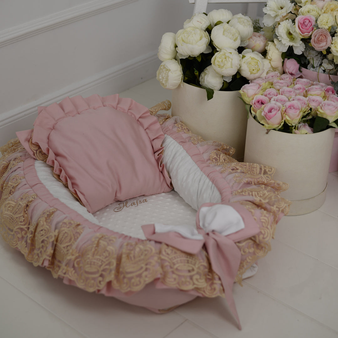 Pink baby nest with ruffles and pillow, flowers in the background