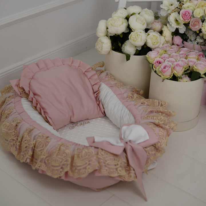 Pink baby nest with ruffles and pillow, flowers in the background