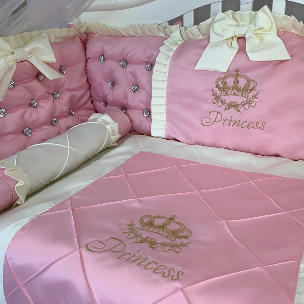 Pink baby crib bumpers with rhinestones set with 'Princess' embroidery and decorative bows.