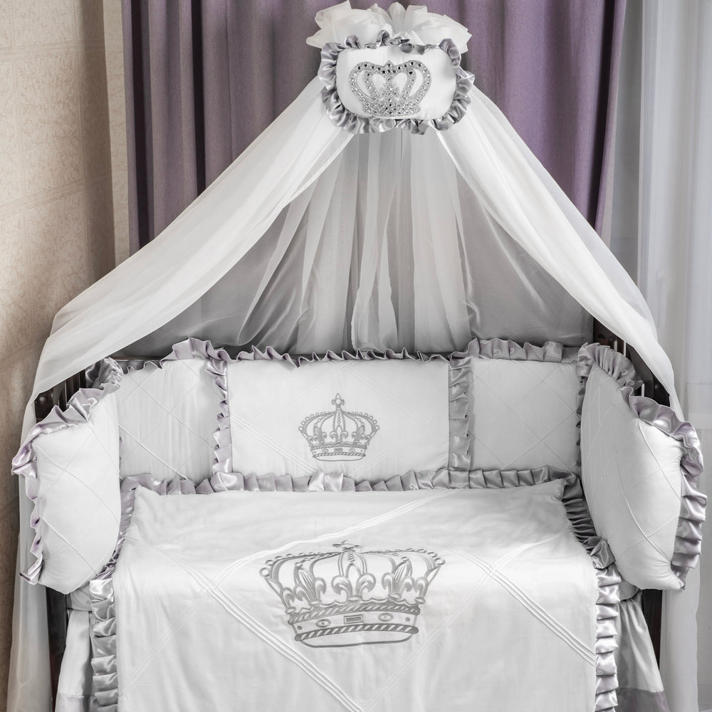 White crib set with embroidered crowns and canopy in a nursery setting.