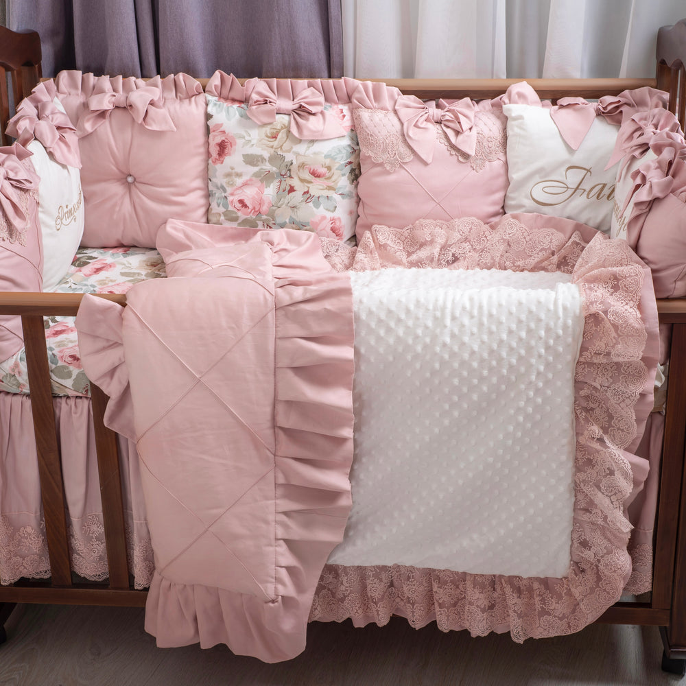 Pink satin crib set with ruffles and floral patterns on a wooden baby crib.