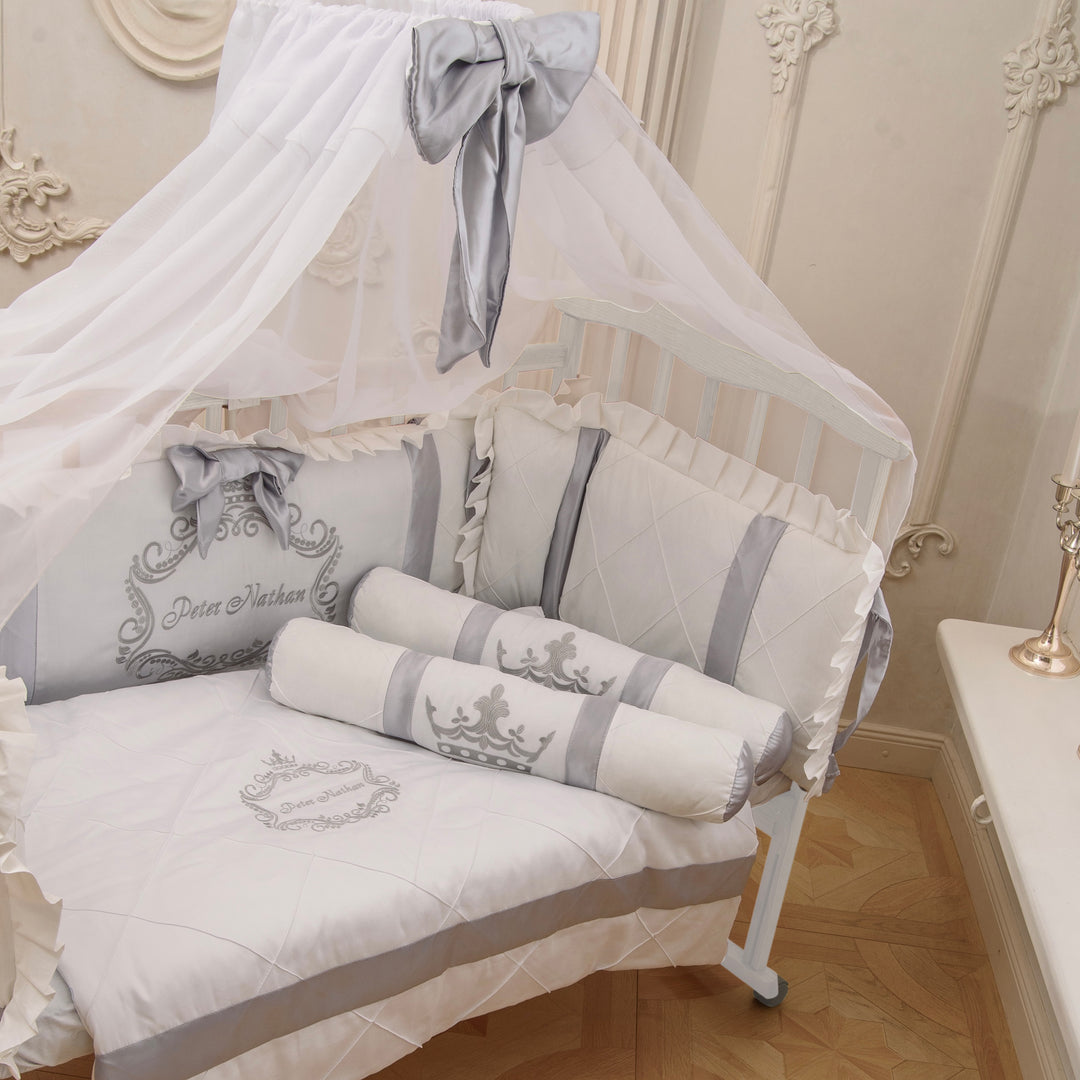 Baby crib with white and gray newborn bedding in a decorated room