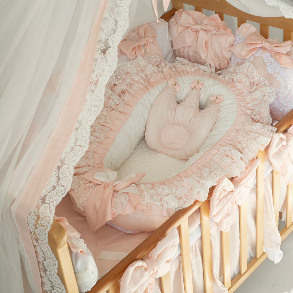 Delicate peach crib set with lace details and baby nest in a baby crib.