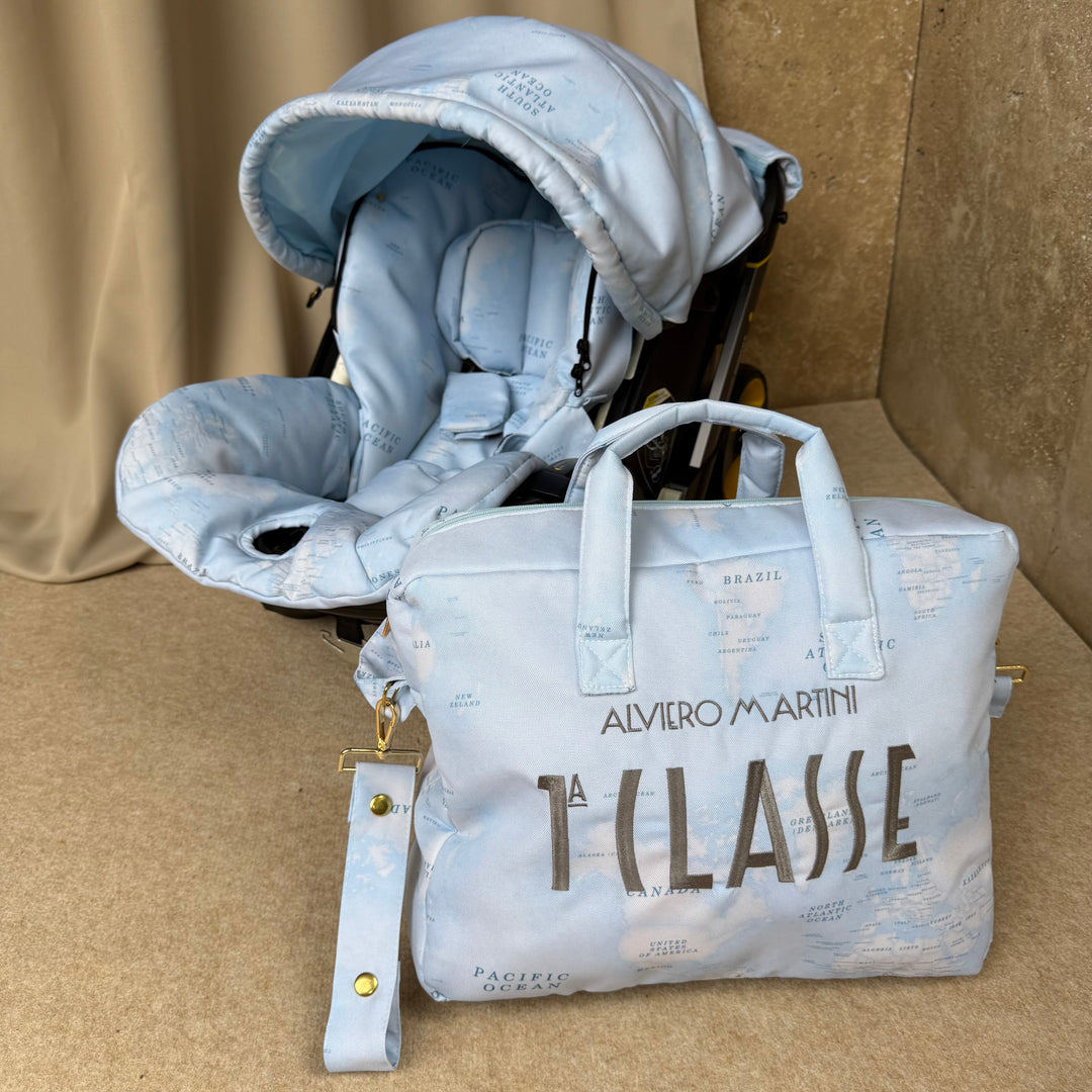 Interior view of Doona + with light blue world map cover set, styled against a beige backdrop, paired with matching diaper bag featuring silver embroidery.