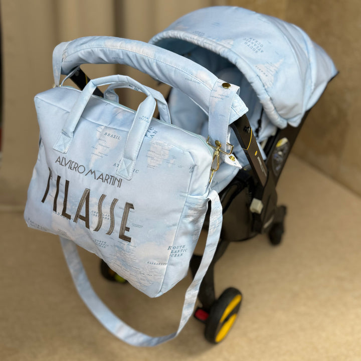 Interior angled view of Doona Plus with light blue world map cover set and matching diaper bag with silver embroidery attached to the handlebar.