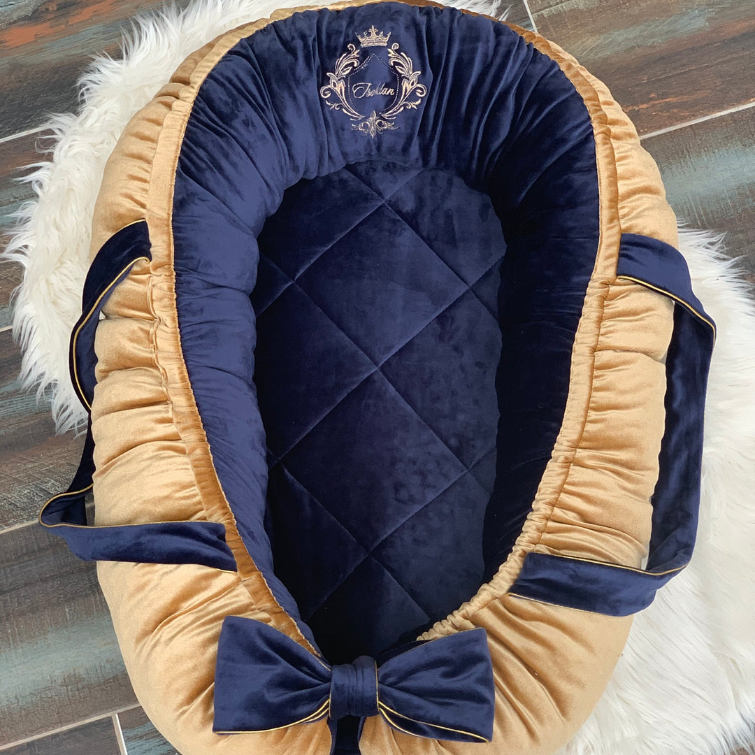 Navy blue and gold velvet baby nest with a bow on a textured surface