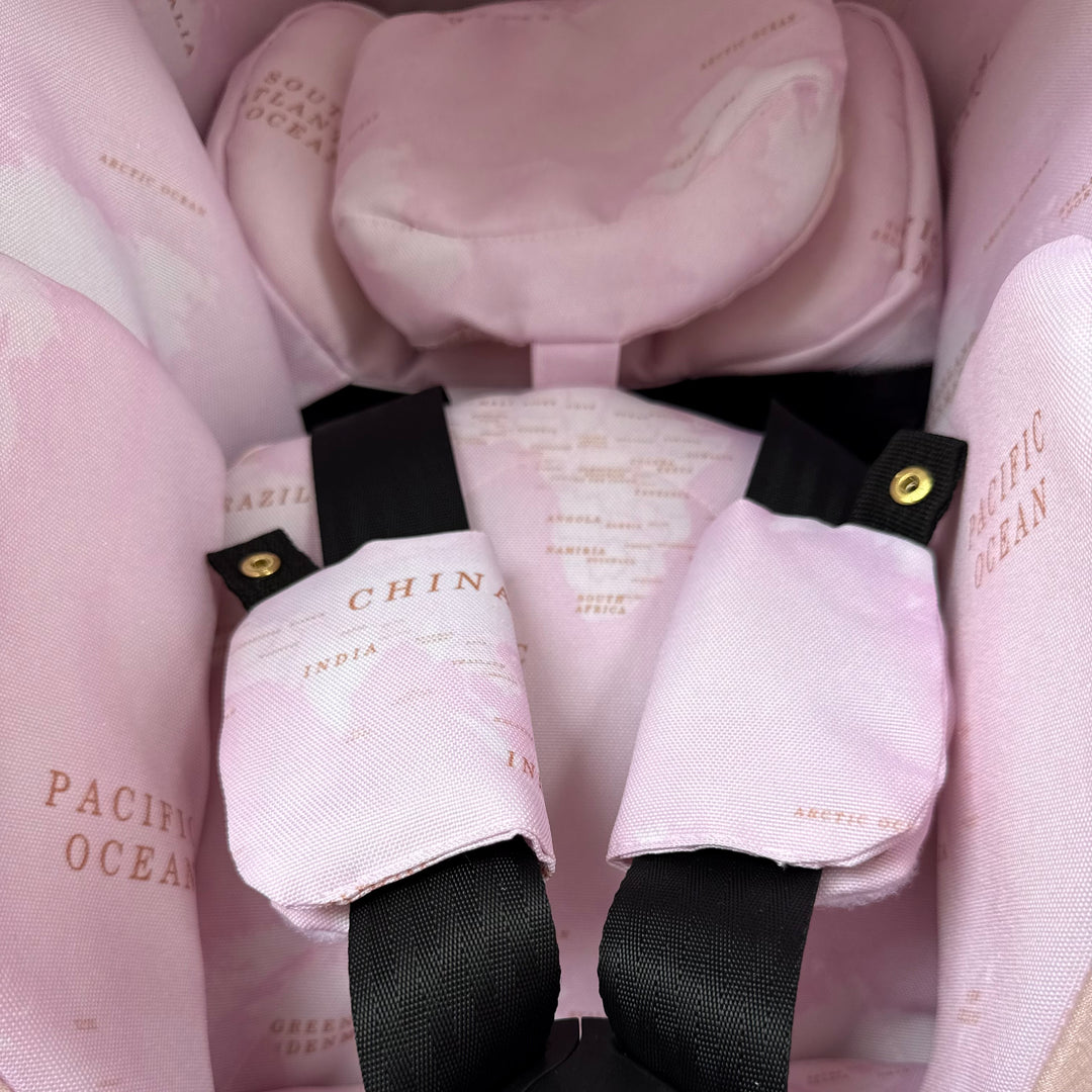 Close-up of pink world map car seat cover interior on Doona X featuring infant insert, head support and padded shoulder strap covers.