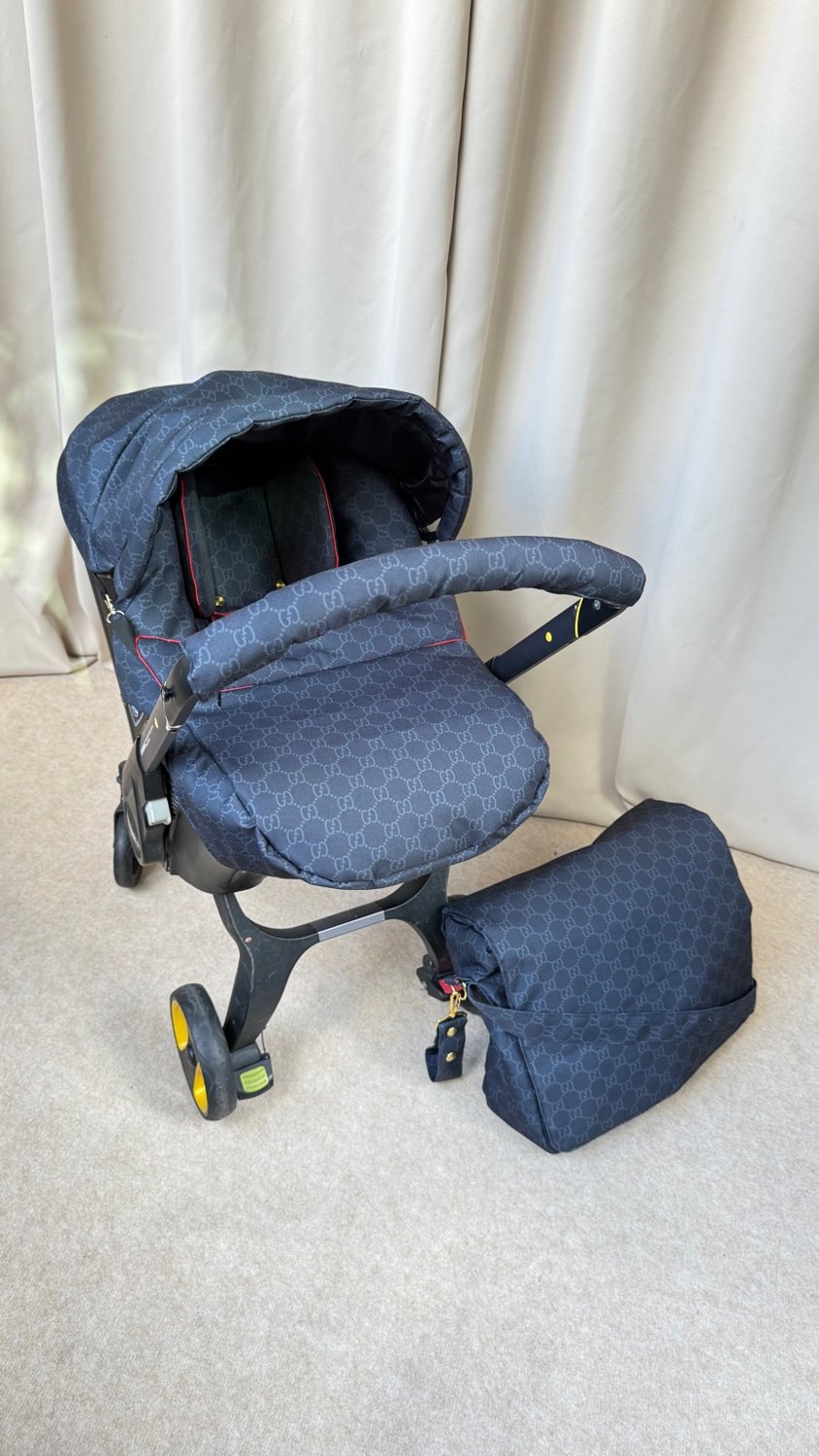 Infant car seat with black luxury-inspired monogram fabric cover, padded seat insert and matching black diaper bag placed next to the car seat on a neutral background.