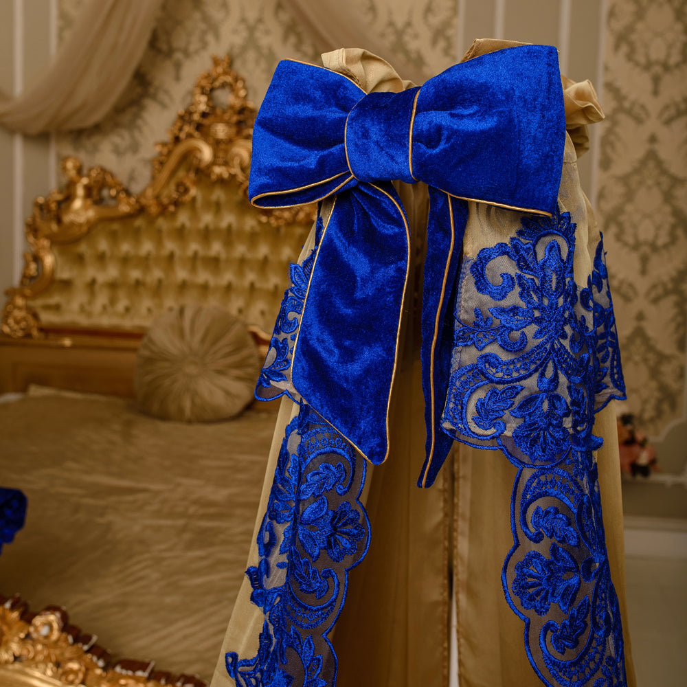Decorative gold canopy with a large blue bow and intricate royal blue lace details in a bedroom setting.