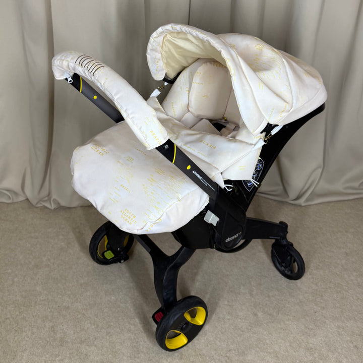 Beige world map car seat cover set installed on Doona Plus, angled side view on neutral curtain background.