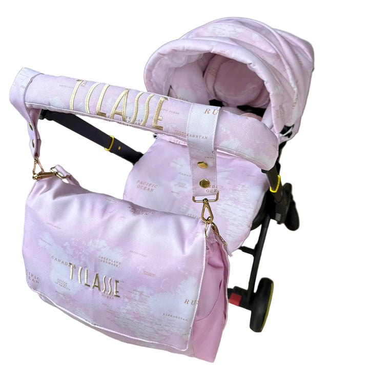 Rear angled view of pink world map cover set installed on Doona X car seat, featuring embroidered handlebar cover and matching diaper bag with gold lettering.