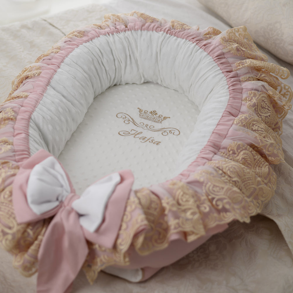 Delicate pink baby nest with gold lace and bow details on a soft surface