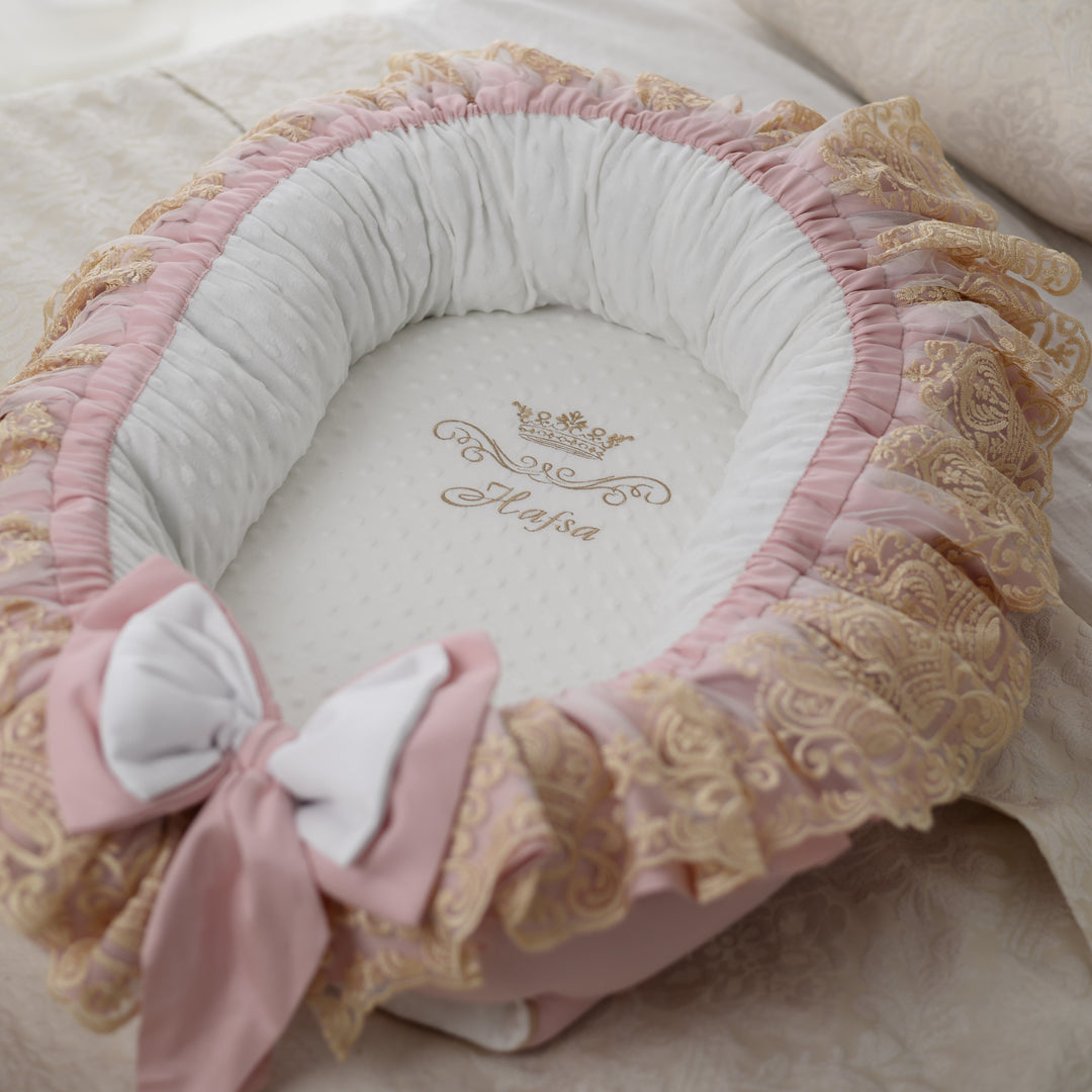 Delicate pink baby nest with gold lace and bow details on a soft surface