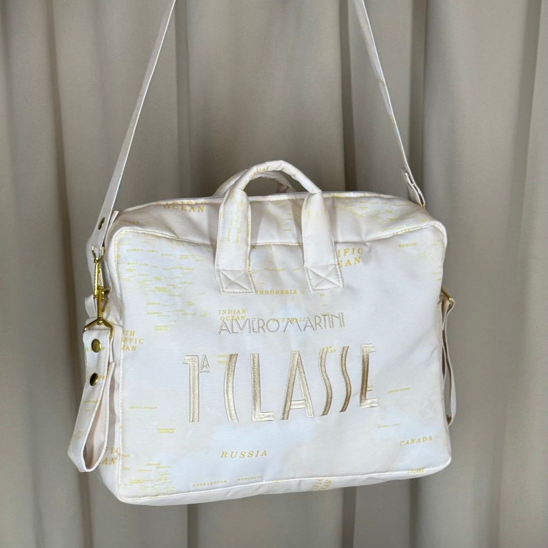 Beige world map diaper bag with gold embroidery on curtain background.
