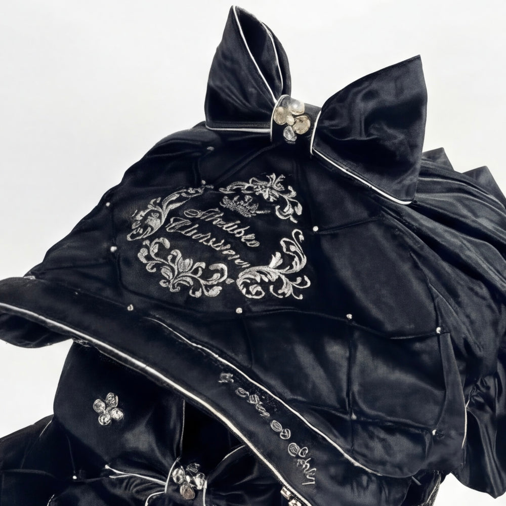 Close-up of a black velvet car seat canopy featuring an oversized decorative bow, rhinestone accent, and embroidered crest detail