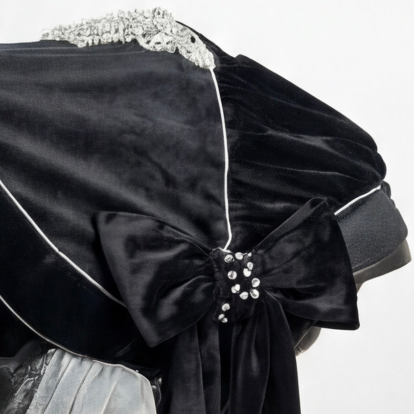 Close-up of a black velour canopy installed on a baby car seat, featuring an elegant oversized bow accented with a rhinestone brooch. The canopy is finished with refined decorative piping, subtle lace detailing along the top edge, and a soft velour fabric with a gentle sheen. The image is photographed on a clean white background.