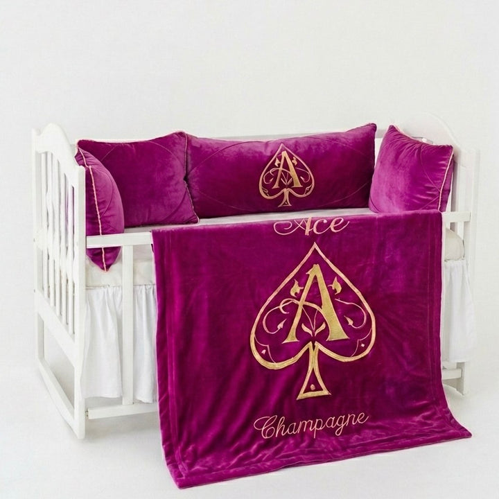 Purple velvet baby crib set with gold 'Ace of Spades' design on a white crib