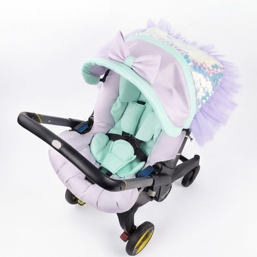 Mermaid-inspired baby car seat cover on a Doona car seat with mint and lavender padded inserts and a tulle ruffle canopy, photographed on a white background.