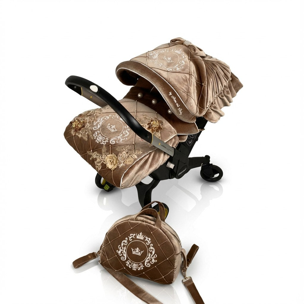 Side view of a Doona car seat on a light background, featuring a brown velvet canopy and matching velvet footmuff with quilted panels, embroidered crest motifs, lace appliqués, pearl details, and decorative brooch accents. A coordinated quilted bag with embroidered emblem is placed in front.