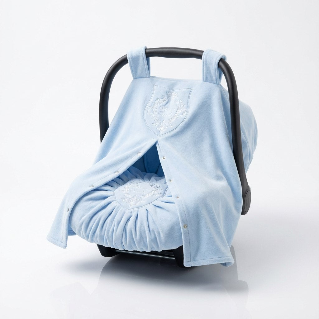 Soft light blue plush baby car seat cover with white embroidered detailing, featuring a padded interior and wrap-style front panels. The plush fabric creates a cozy texture, photographed on a clean light studio background.