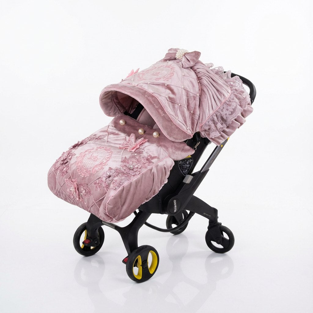 Side view of a Doona car seat shown on a light background. The set features a dusty pink velvet canopy and matching velvet footmuff with quilted panels, lace ruffles, decorative bows, pearl accents, and embroidered crest details. Black frame with integrated wheels visible.