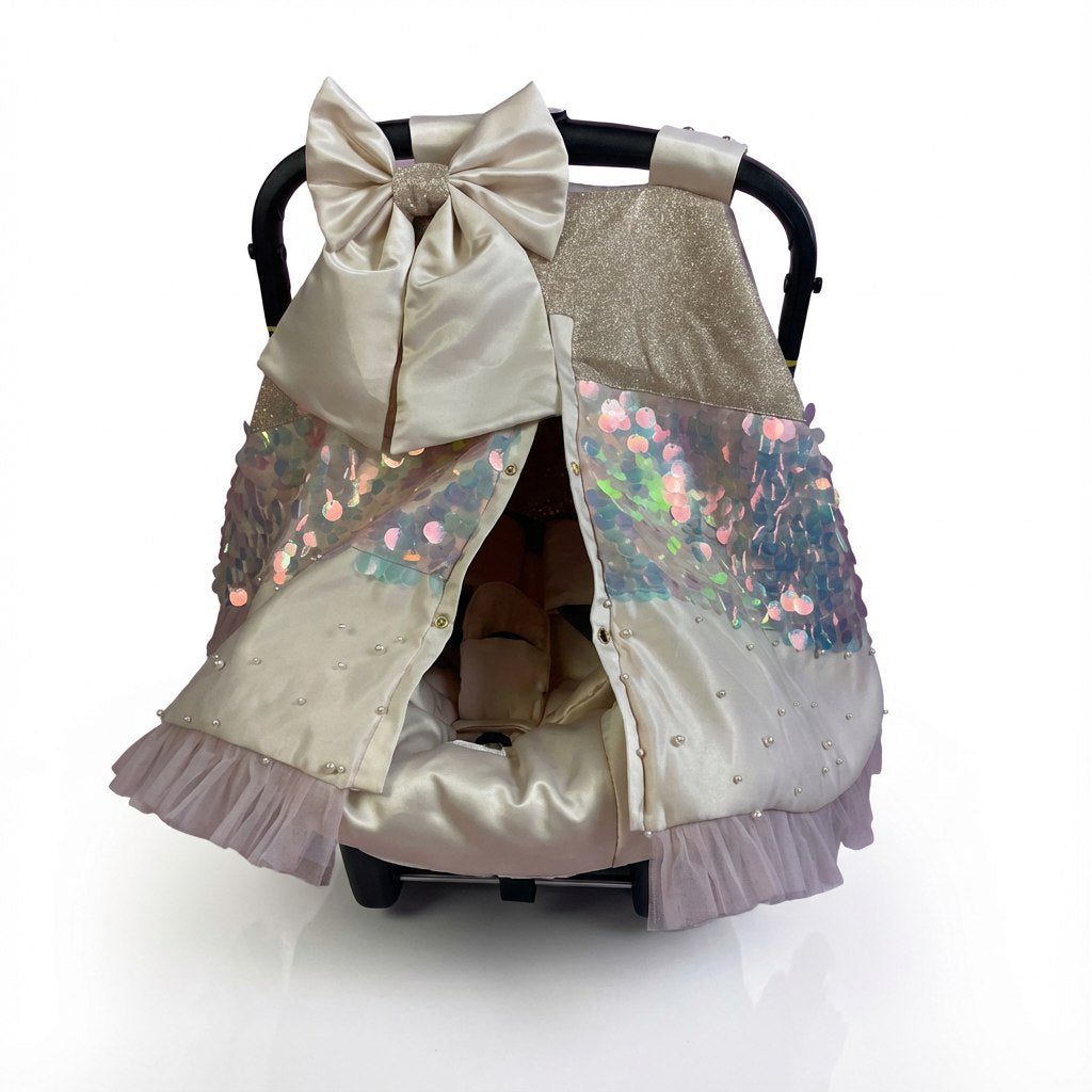 Elegant baby car seat cover set in champagne and ivory tones, featuring a large satin bow on the handle, sequined panels, delicate bead detailing, and soft ruffled trim. Luxurious decorative design photographed on a clean light studio background.