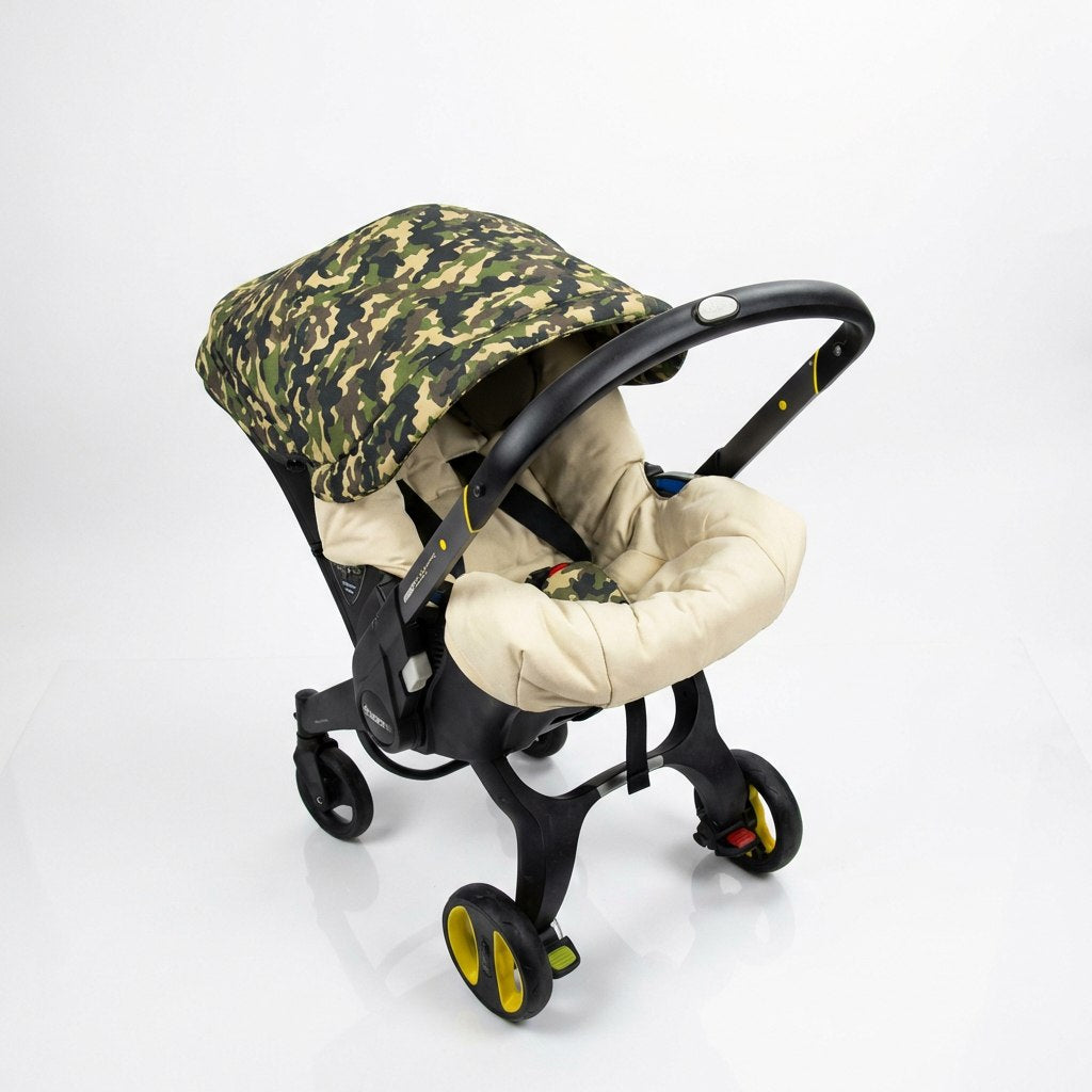 Baby car seat cover on a Doona car seat with a camouflage canopy and beige padded seat insert, photographed on a white background.