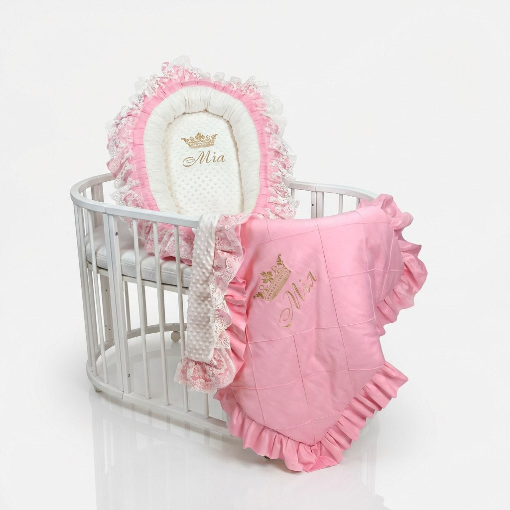 Pink baby nest and blanket set with 'Mia' branding on the crib with a white background