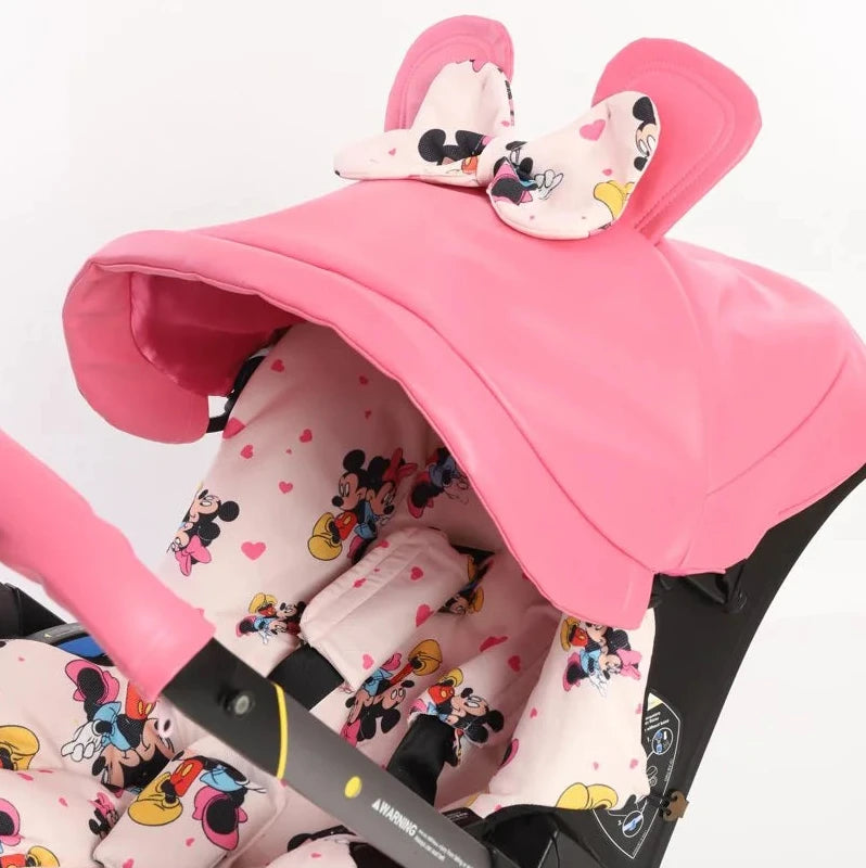 Pink baby car seat cover set with 3D cartoon ears canopy and pastel character print, installed on Doona+ infant car seat.
