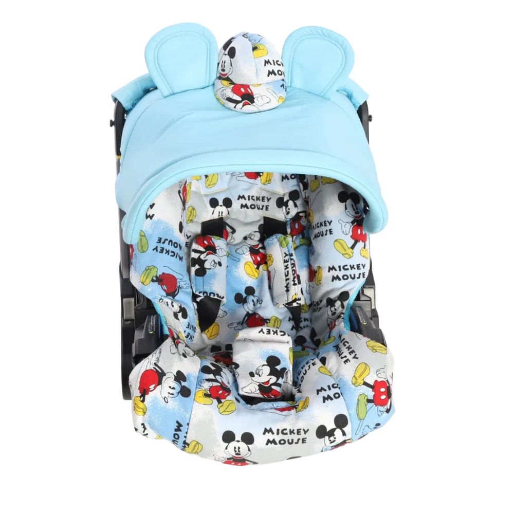 Front view of a baby car seat with a light blue canopy installed, photographed on a white background. The canopy has a rounded shape with two decorative bunny ears and a small central patch made of Mickey Mouse printed fabric. Inside the car seat, the seat liner, shoulder pads, and crotch pad feature an all-over Mickey Mouse print in black, red, yellow, and light blue on a white background. The car seat frame is partially visible on both sides.