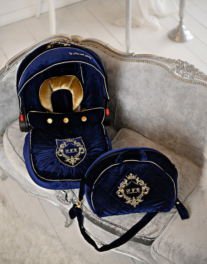 Image of royal blue velvet baby car seat cover set for Graco, embellished with gold personalized embroidery on the hood, footmuff, and diaper bag. The set is accented with luxurious gold elements, including the baby insert, trim around the cover, and diaper bag. Matching accessories such as the blanket complete the elegant ensemble.